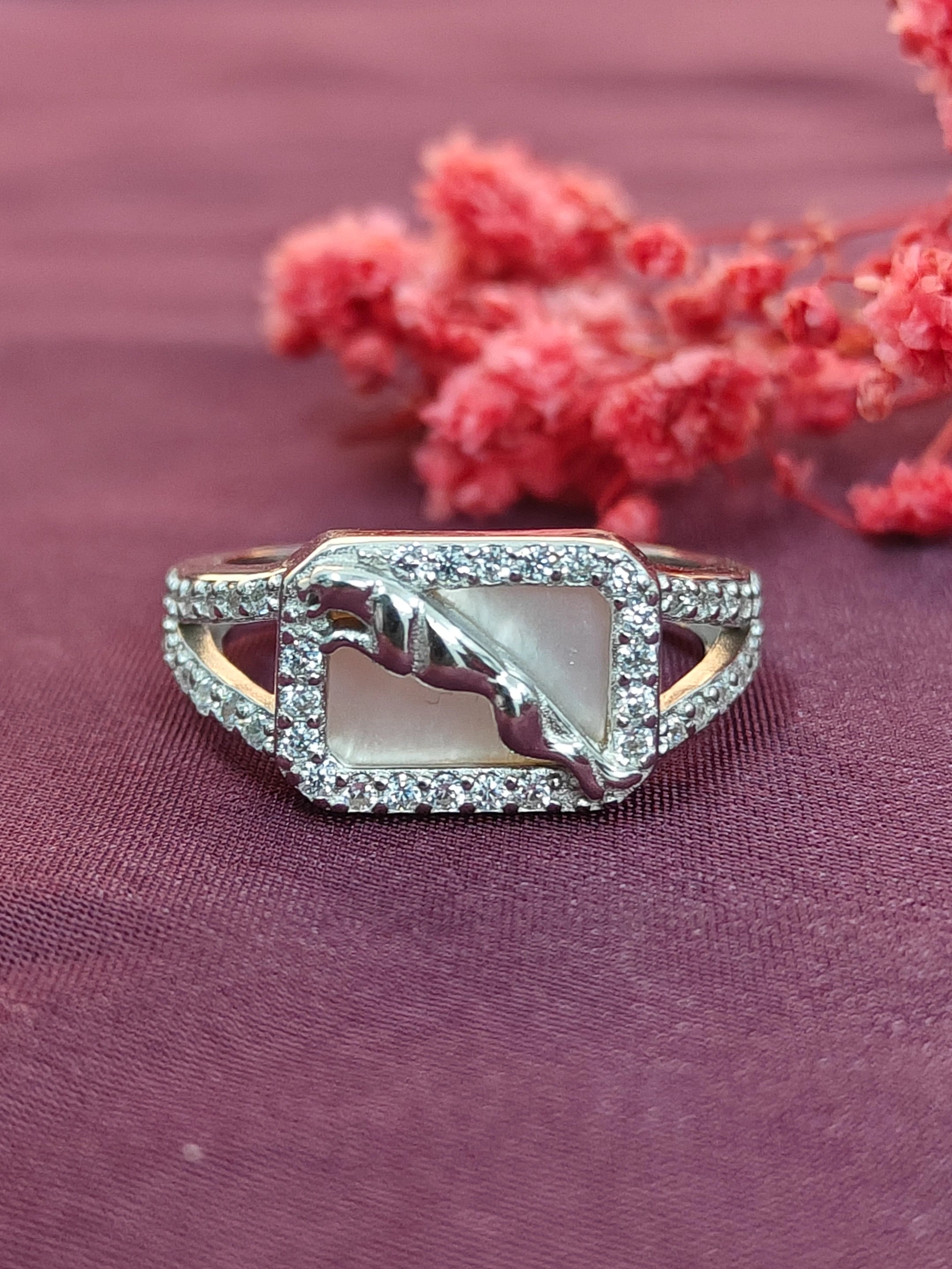 Elegant ring with a central stone and diamond accents on a purple fabric background with pink flowers.